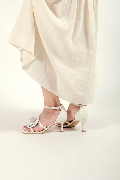 Lifestyle view of a woman wearing ivory floral kitten heel sandals with a flowing cream midi skirt.