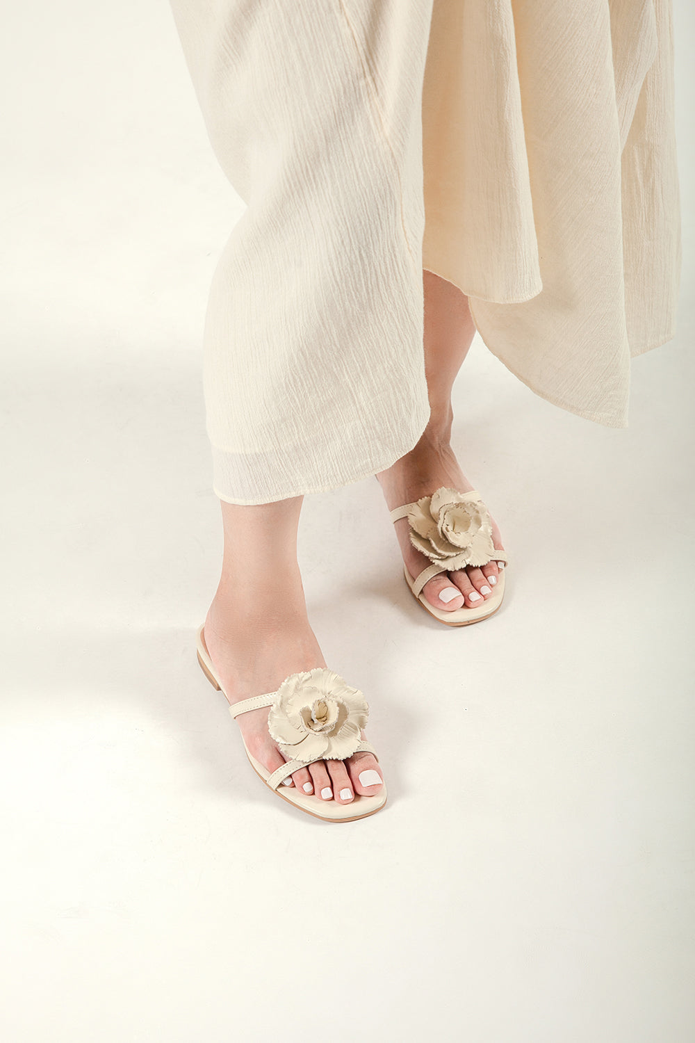 Lifestyle view of a woman walking in beige leather flower slides and a flowing linen skirt.