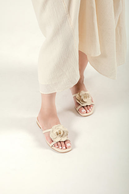 Lifestyle view of a woman walking in beige leather flower slides and a flowing linen skirt.