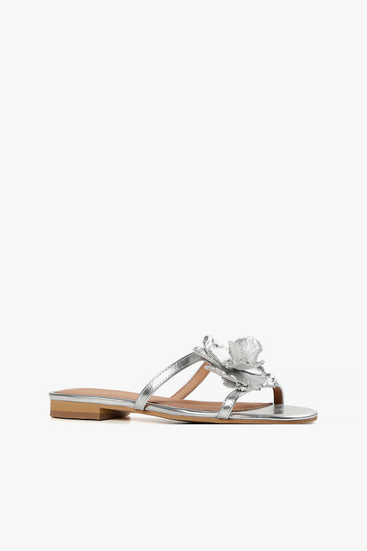 Women's metallic silver leather slide sandals with a large handcrafted 3D floral accent and flat sole.