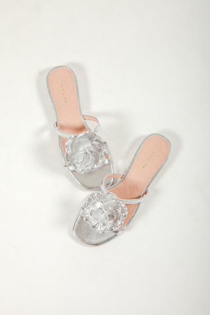 Top down view of a pair of ALL BLACK silver metallic flower slides with nude leather lining on a white background.