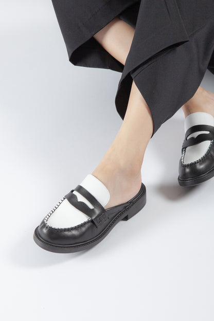 black and white leather penny loafer mule with contrast vamp and moc toe stitching, women’s low heel slip-on dress shoe styled with tailored pants for modern fall fashion