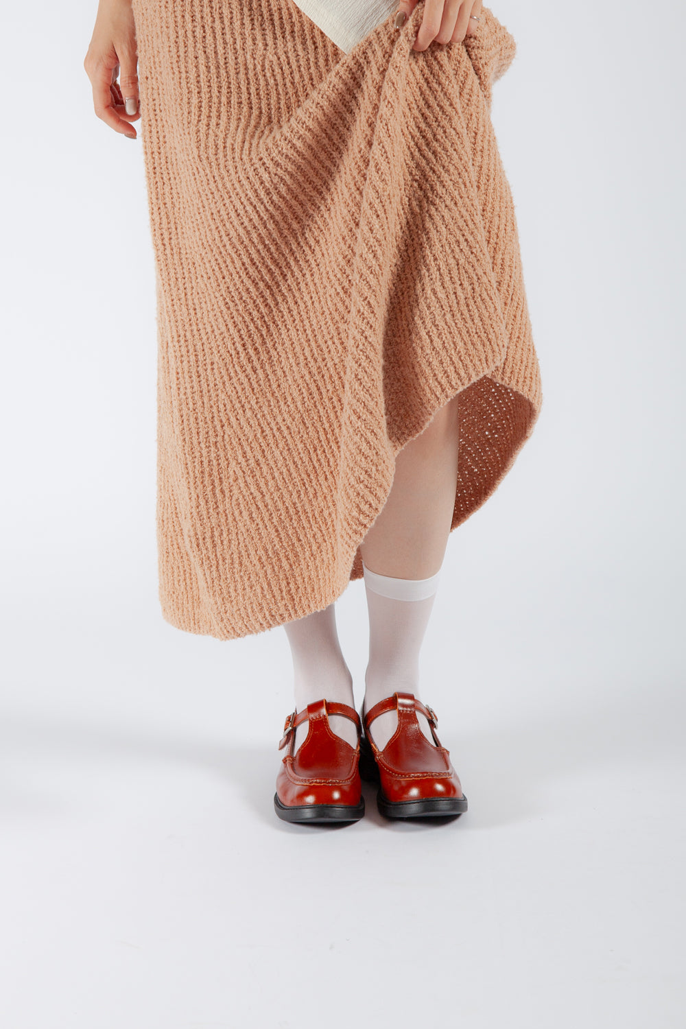 Front view of a woman wearing brown T-strap Mary Janes with white sheer socks and a knit skirt.
