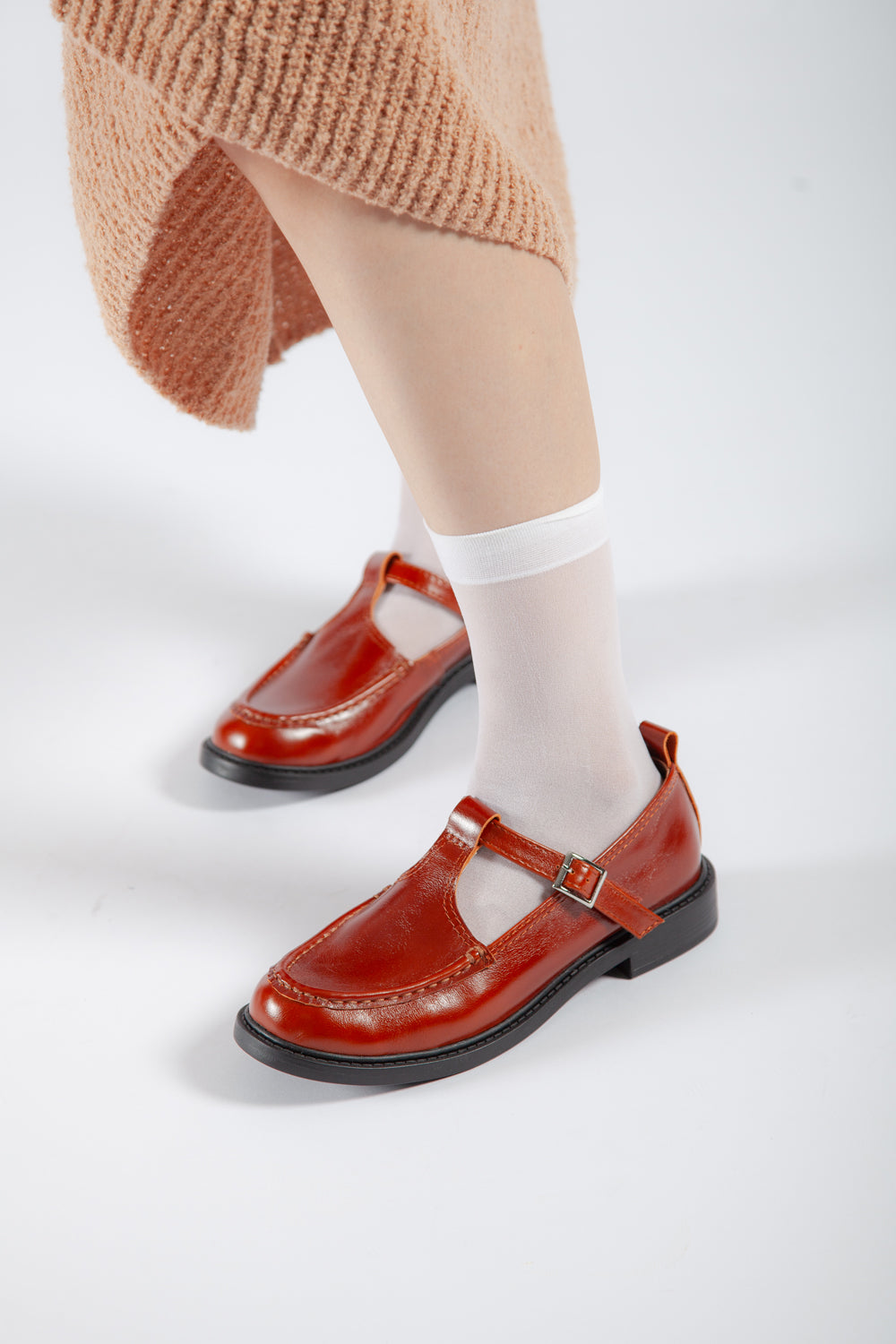 Close-up of women's brown leather buckle shoes on feet, highlighting the T-strap design and black low heel.