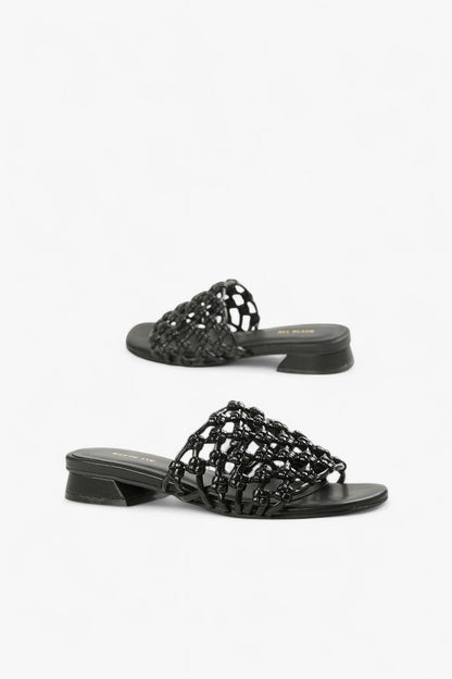 Pair of women's all-black leather slides featuring an intricate 3D square weave strap and low heel.