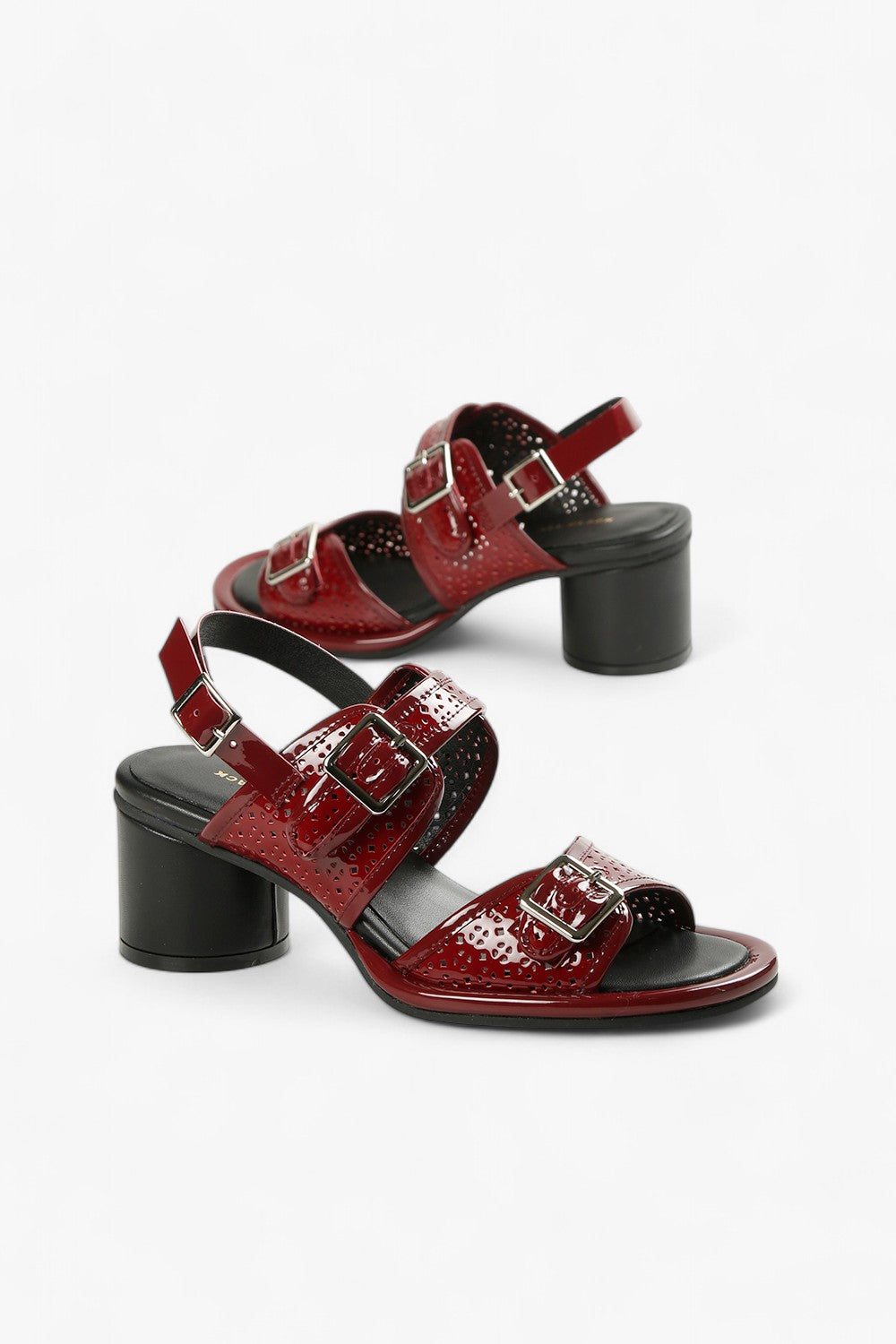 Pair of women's dark red glossy leather heels featuring three adjustable buckles and a modern cylindrical heel.