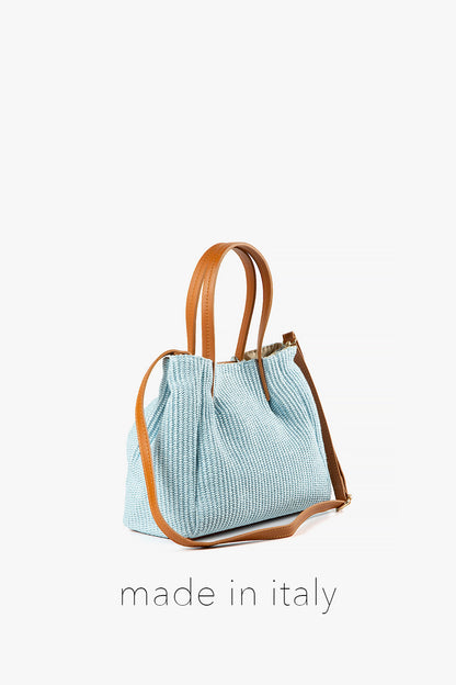 Light blue textured handbag with brown leather straps on a white background, labeled 'made in Italy'.