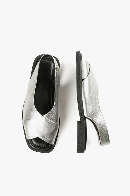 Top and side view of women's silver metallic crossover sandals showcasing square toe silhouette and textured black soles.