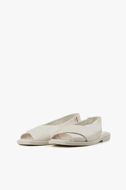 Pair of women's minimalist white open-toe sandals featuring wide crossover leather straps and flat comfort soles.