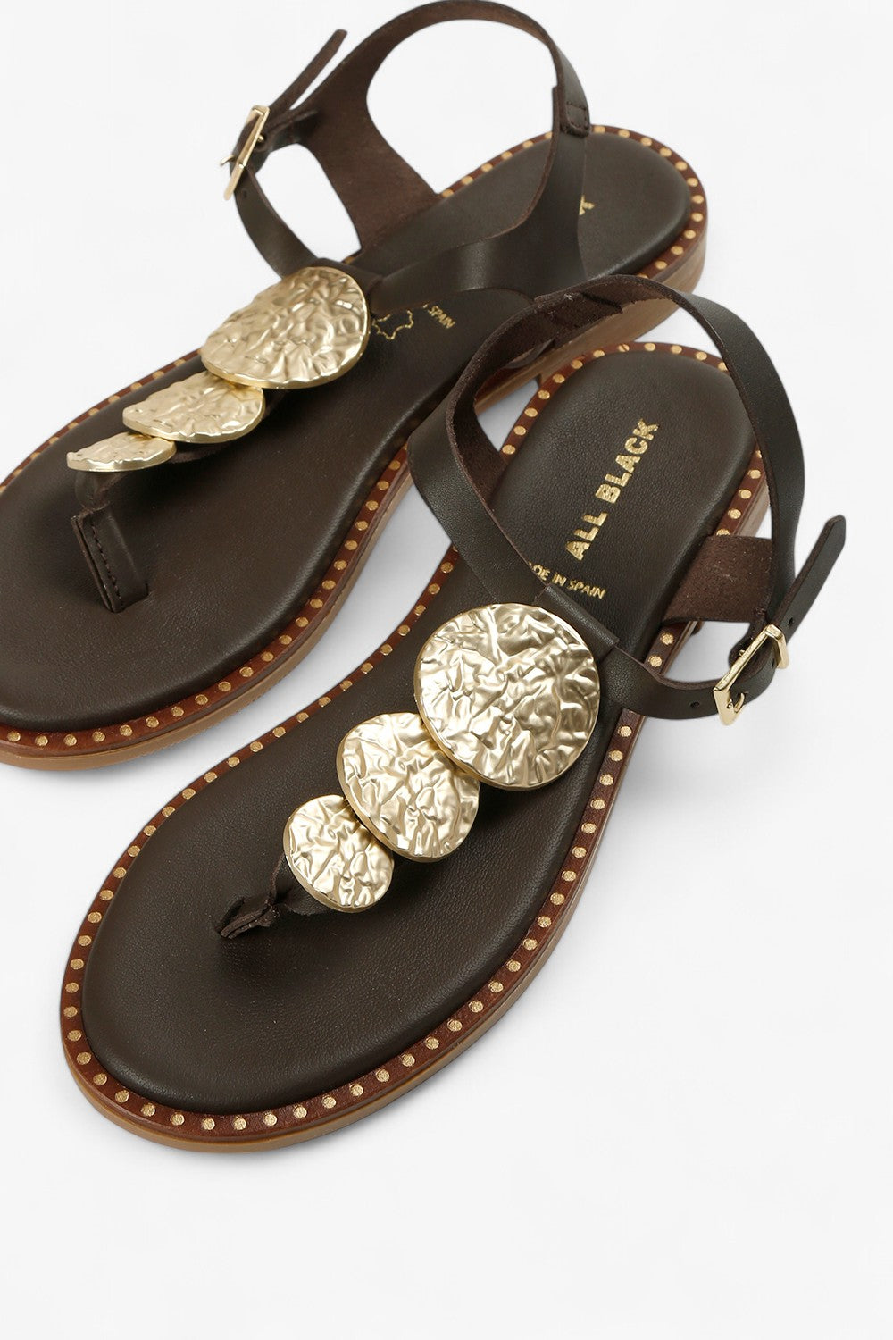 Close-up of women's marron brown sandals featuring textured gold medallions and studded welt detailing.