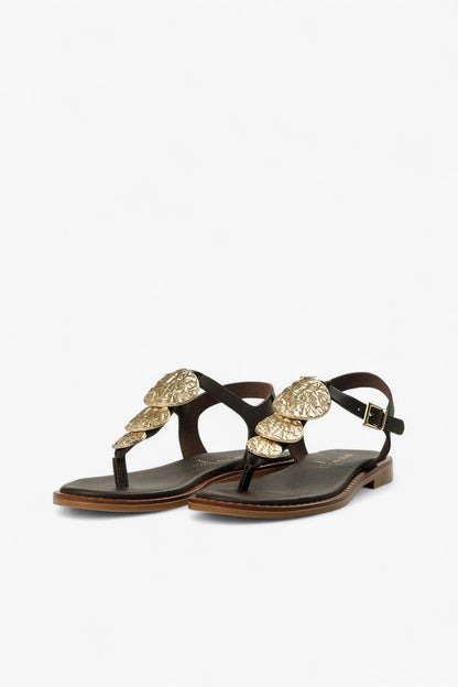 Top down view of women's dark brown T-strap sandals with gold hammered coin accents and gold ALL BLACK logo.