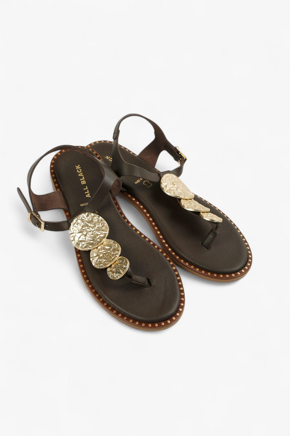 Pair of women's dark brown flat thong shoes with tiered gold hammered discs and slim ankle straps.
